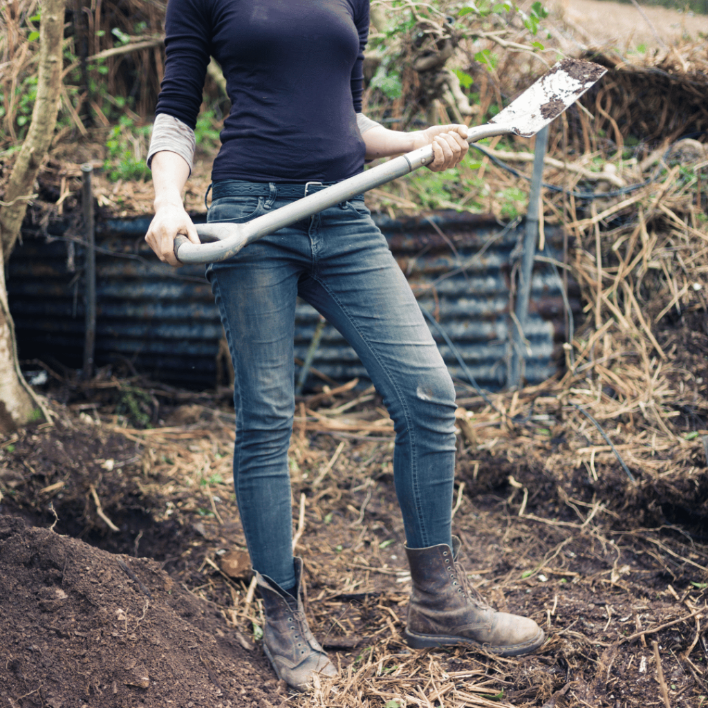 woman in black shirt holding garden spade with raised garden in the background